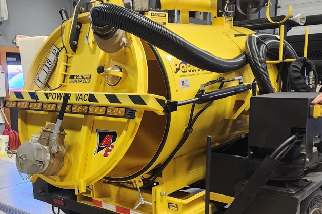 Yellow vacuum truck tank with hose reel and Allied Equipment logo, shown indoors