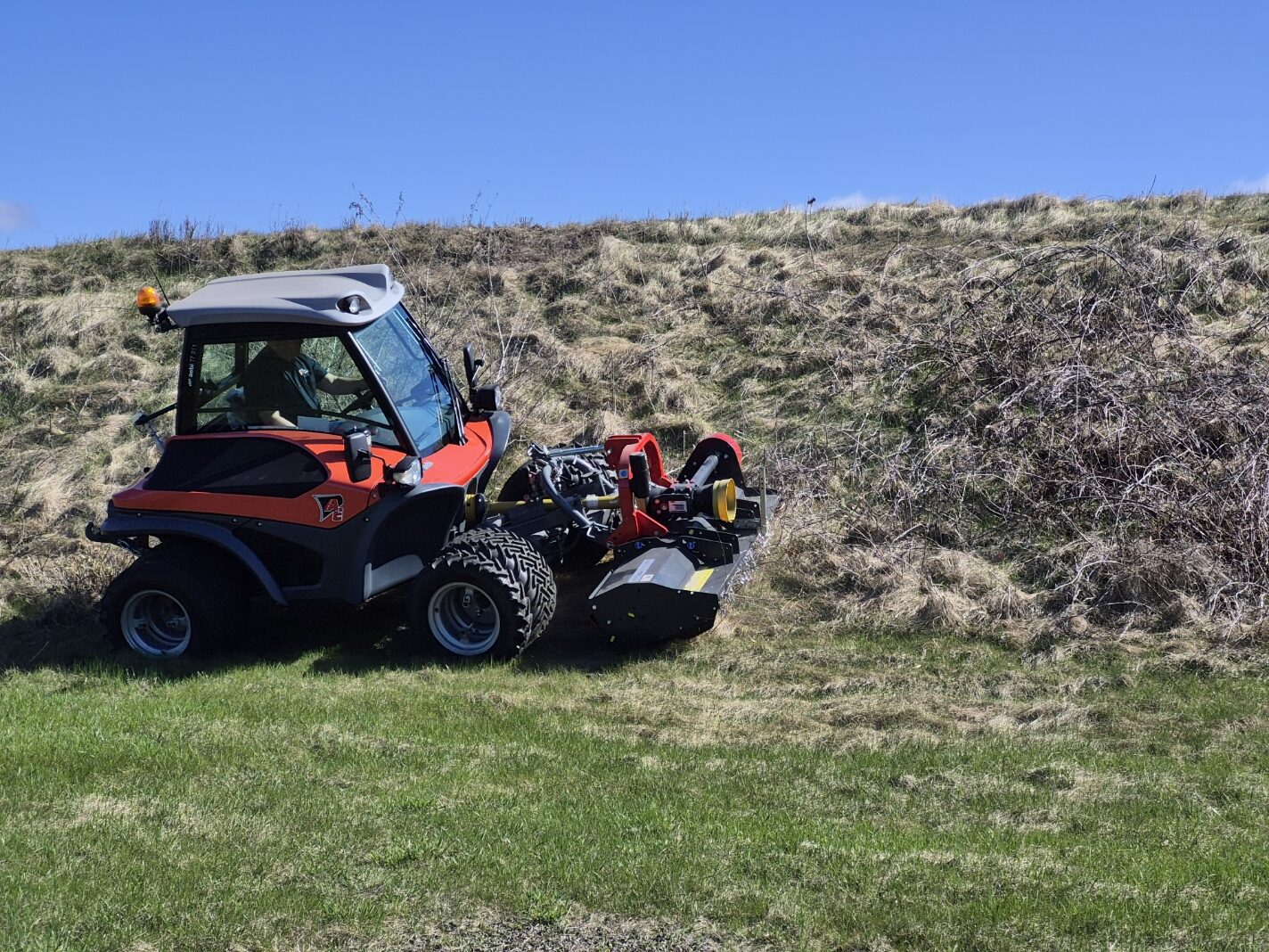 Red and black Aebi slope mower with an operator mowing a grassy embankment