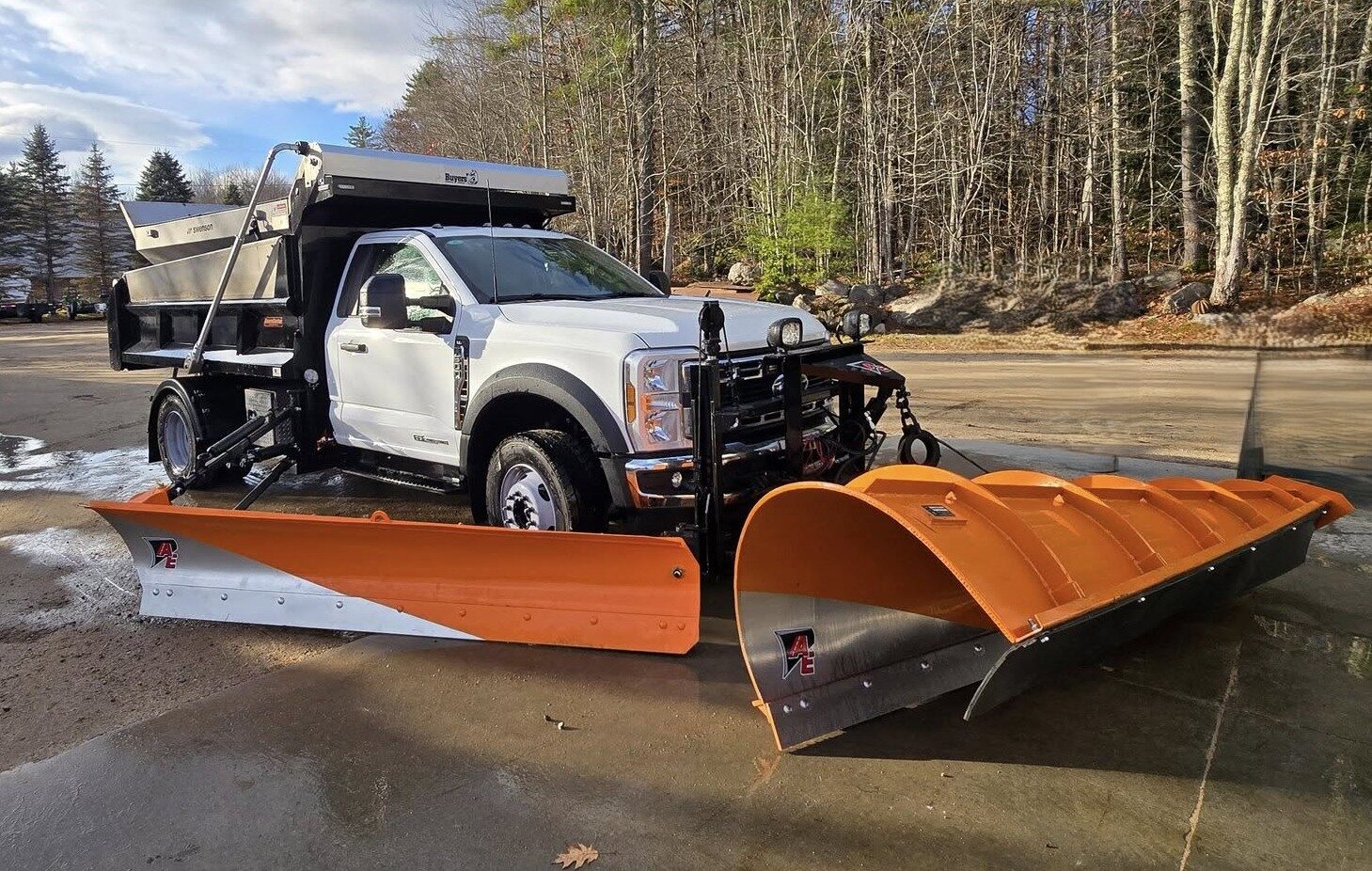 White truck with stainless spreader body, orange front plow and orange wing plow on a wet lot