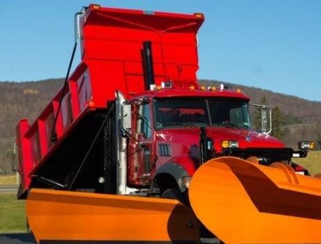Red dump truck with a large orange plow blade and orange wing plow in the foreground