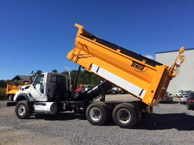 Orange Tenco dump body raised on a white tandem-axle truck, dumping gravel